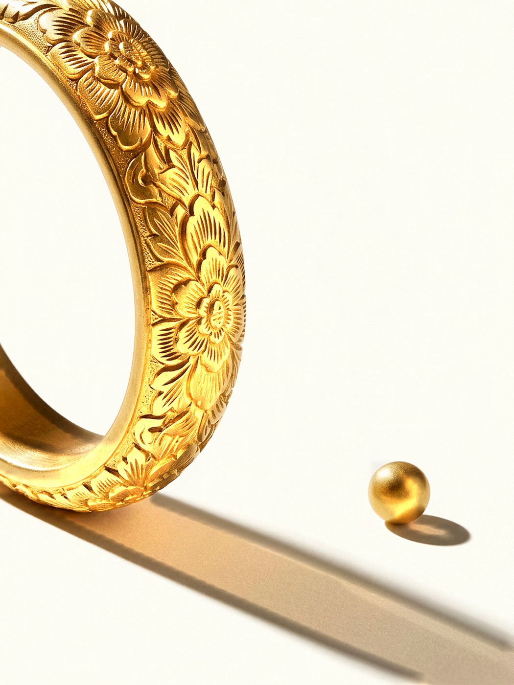 A thick hand-carved gold bangle filling the left of the frame, and a single small gold bead on the right — the bangle melted down.
